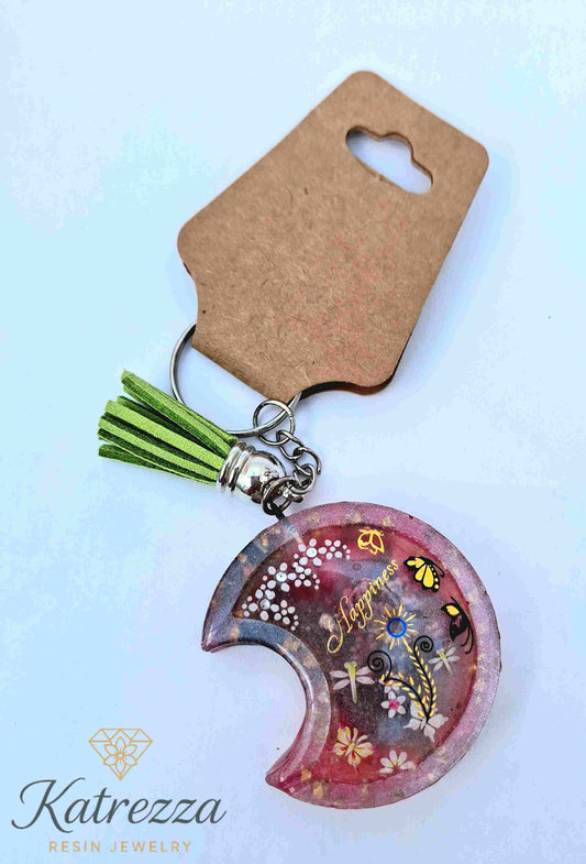 Imperfect resin moon keychain with Happiness text, butterflies, and flowers.