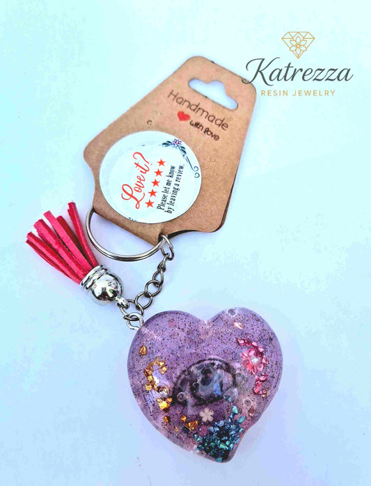 Glittery resin heart keychain with embedded rose and colorful flakes.

