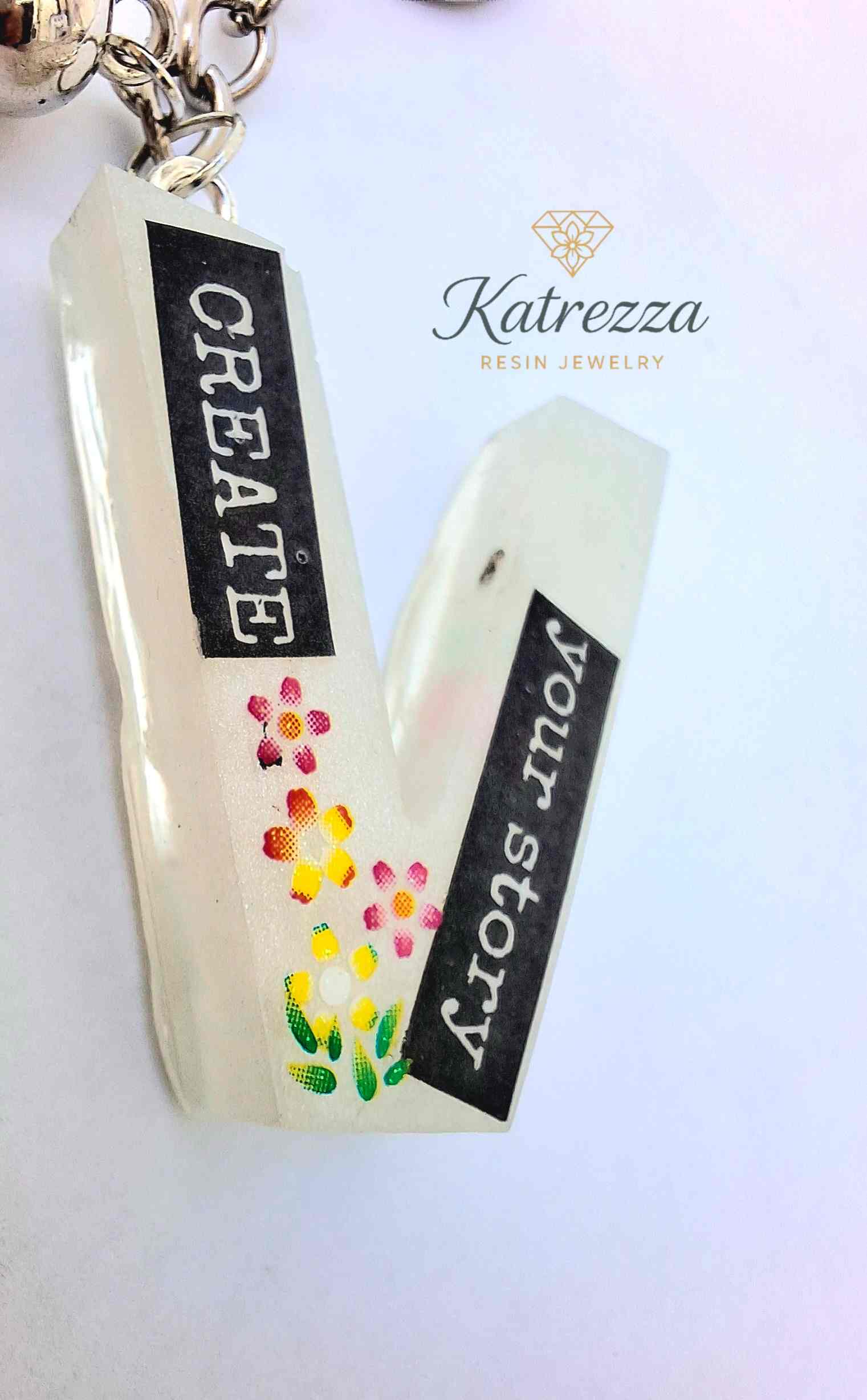 Angled view of resin V keychain with glow effect and floral design.
