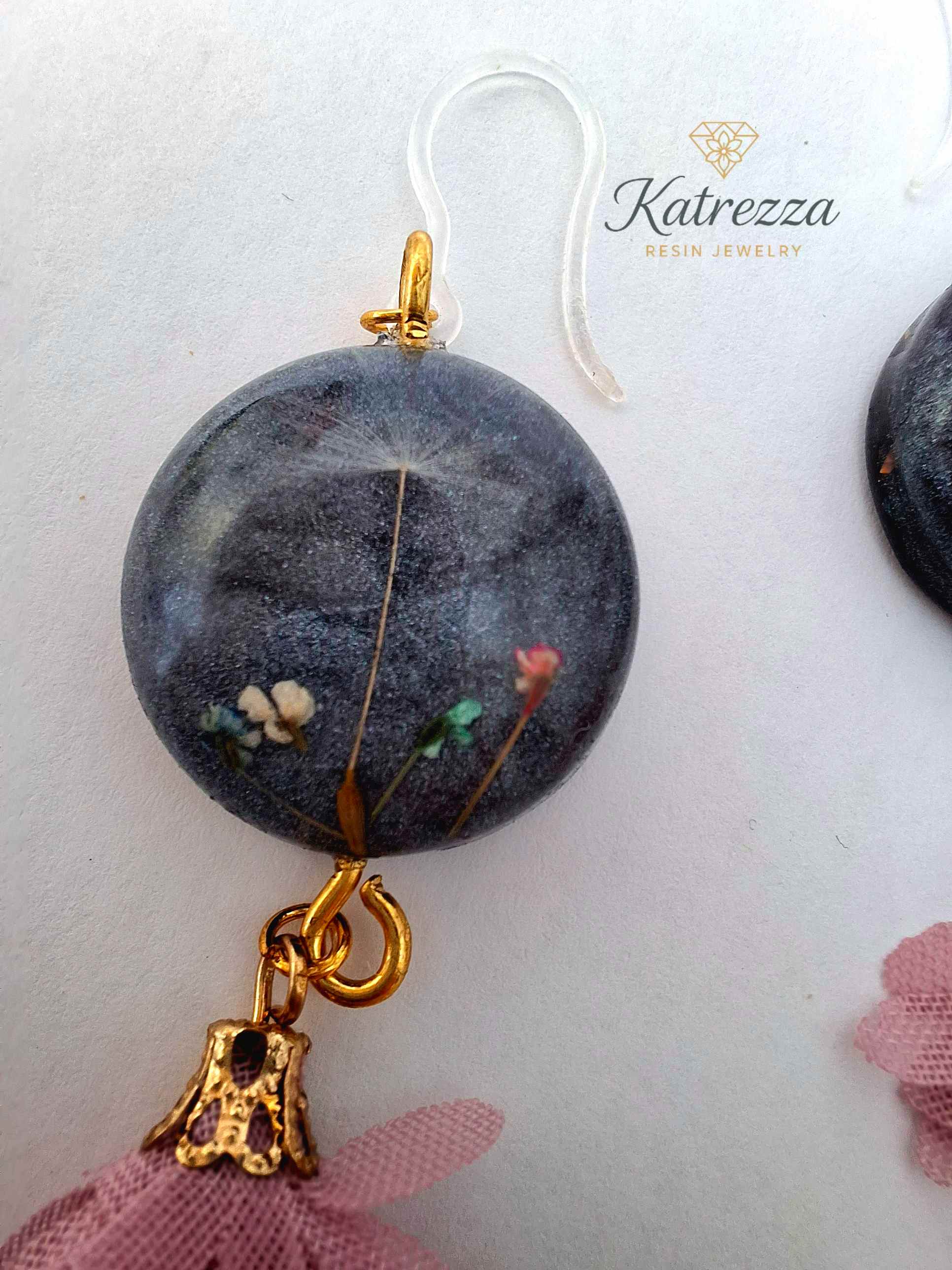“Black resin earring with real flowers and dandelion seed, pink tassel charm, gold accent, and silicone hypoallergenic hook – 6.5 cm length.”