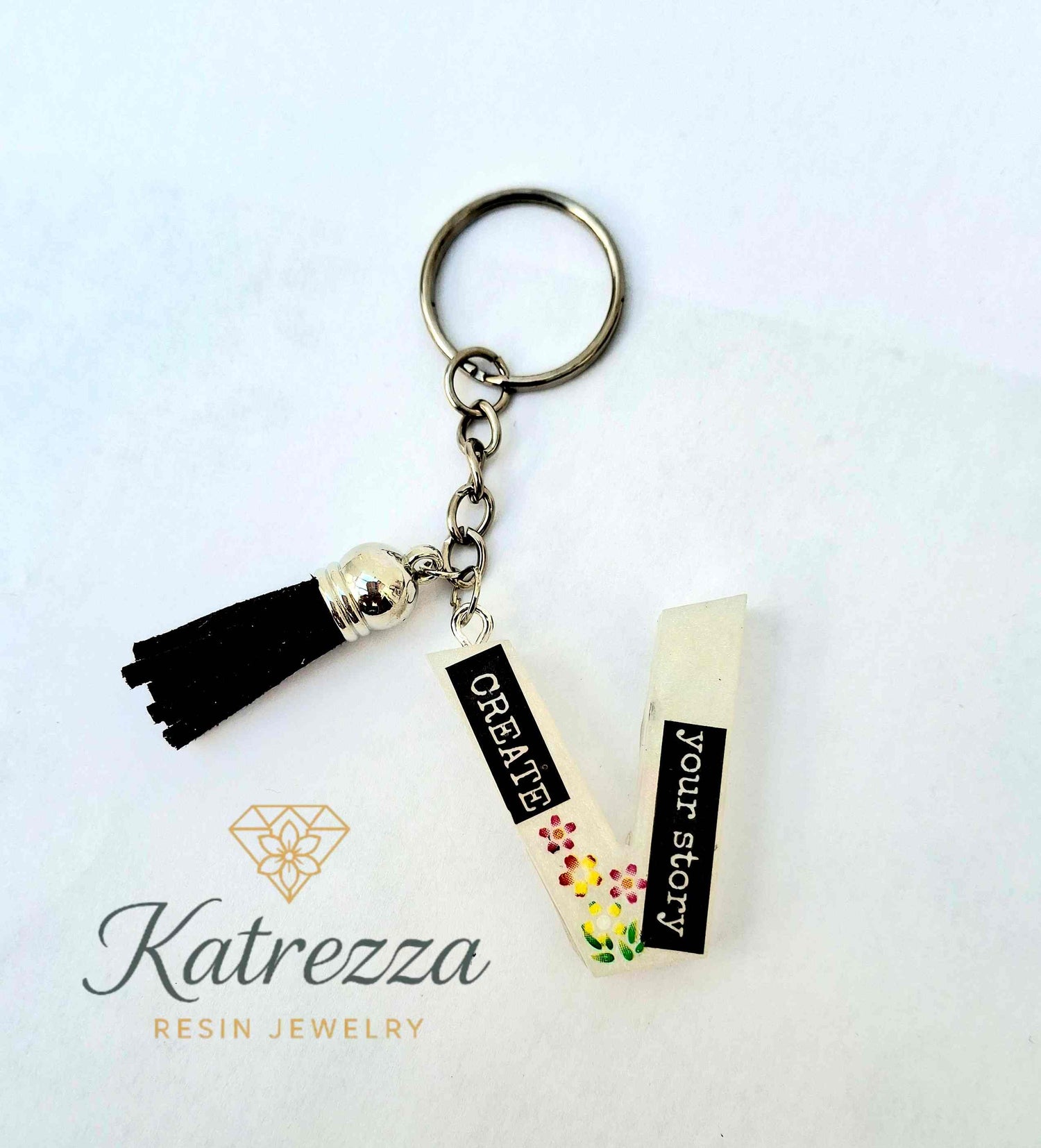 Glow-in-the-dark resin letter V keychain with “Create Your Story” quote and tassel.
