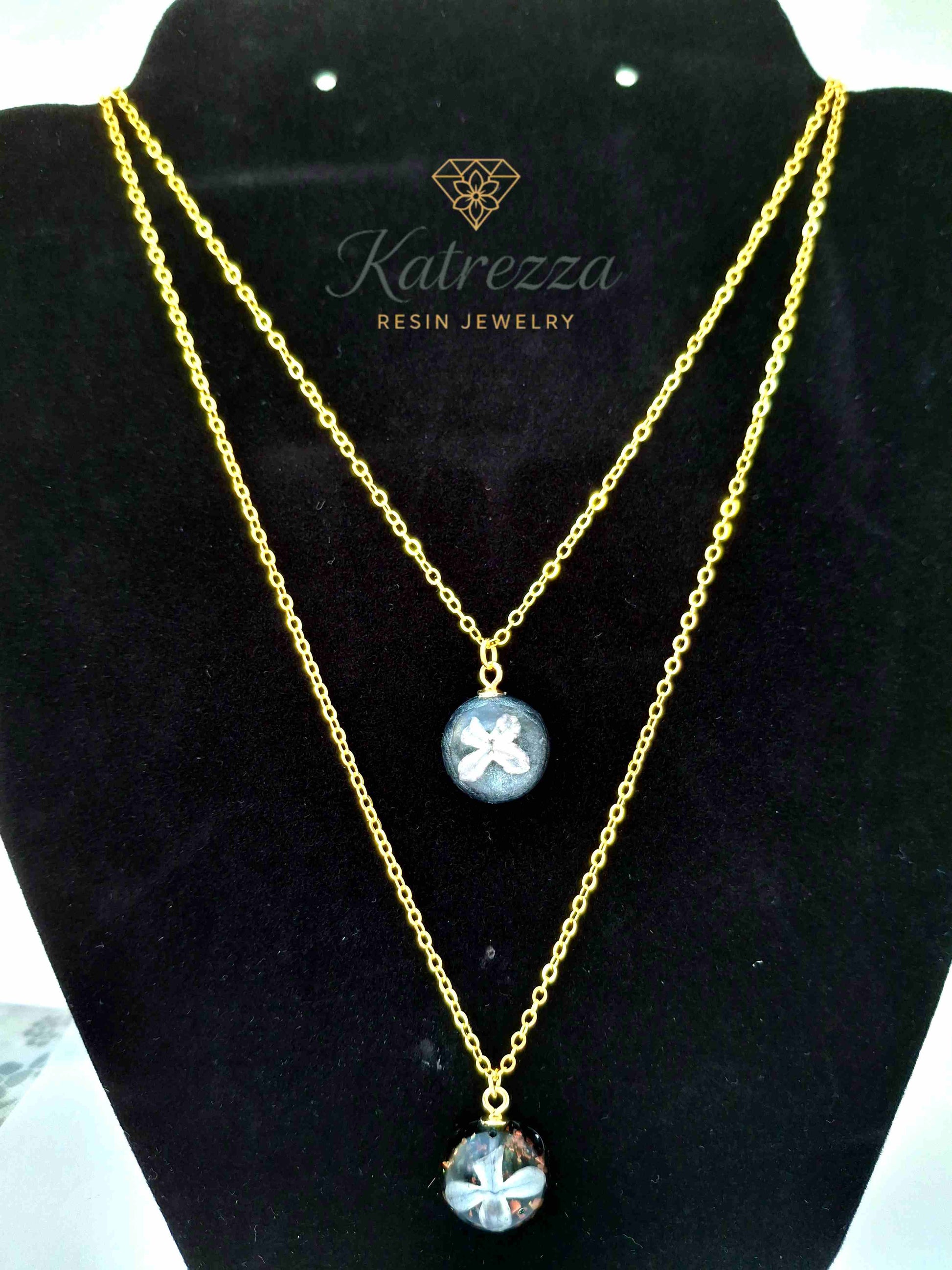 Double pendant resin necklace with real lilac flowers preserved in resin, glitter accents, on a gold double chain – handmade Katrezza jewelry.

