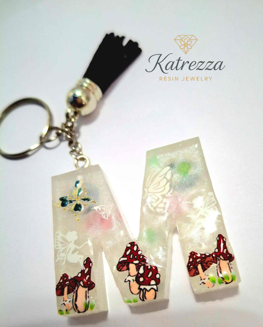 Resin M keychain with fairy, butterflies, and mushroom decorations.

