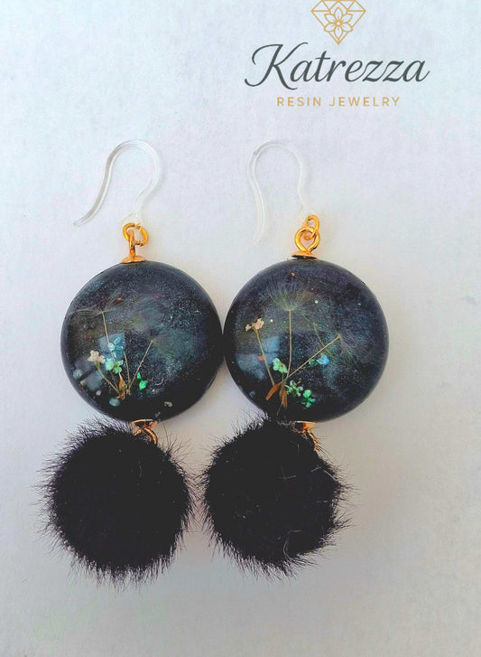“Round resin earrings with real flowers and dandelion seeds in black resin, finished with fluffy black pom-poms and hypoallergenic silicone hooks.”
