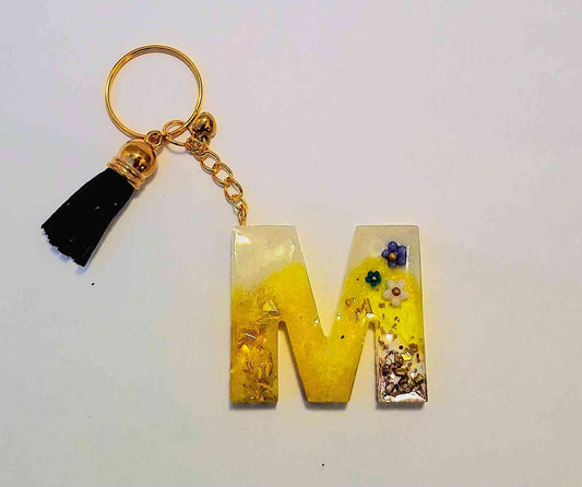 Handmade resin letter M keychain with yellow and floral design.
