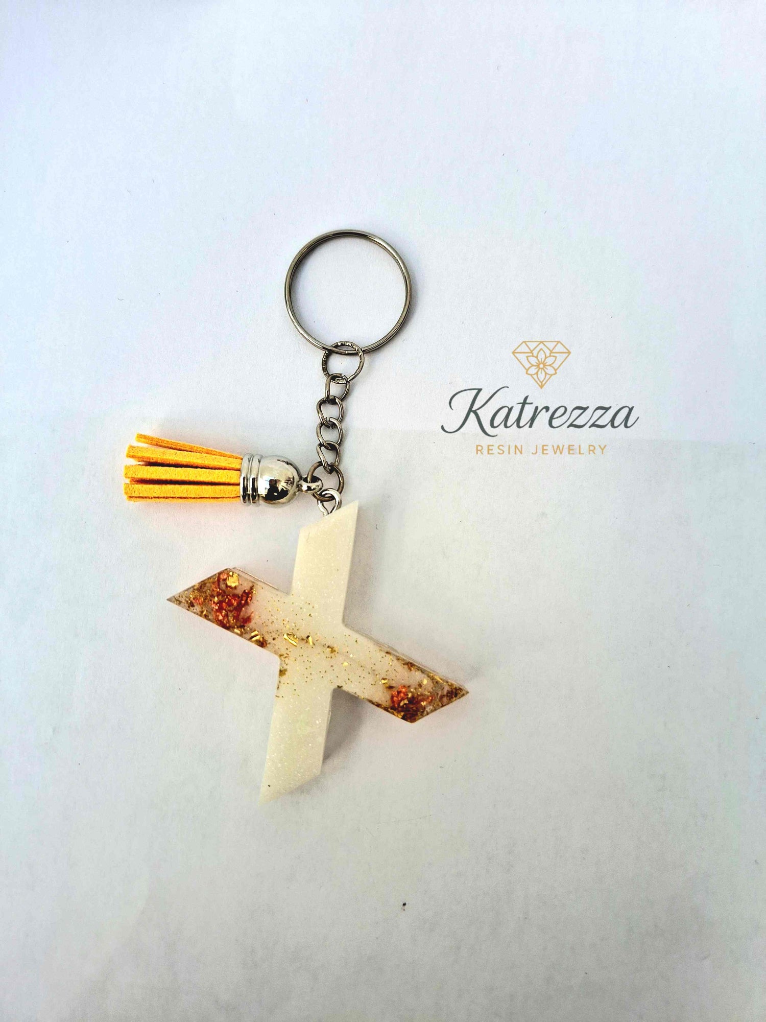 Close-up of resin letter X keychain with gold foil and glitter details.
