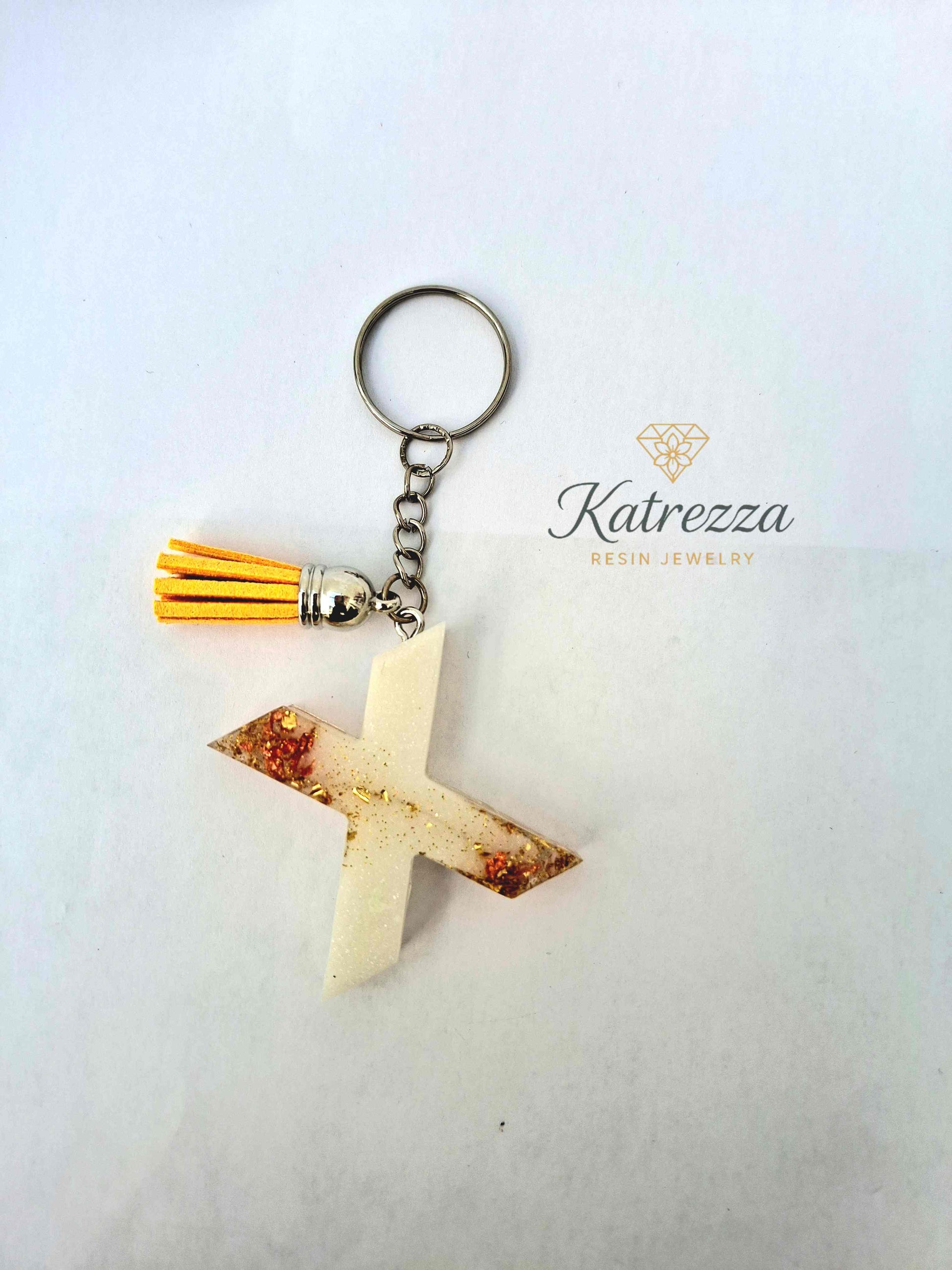 Close-up of resin letter X keychain with gold foil and glitter details.
