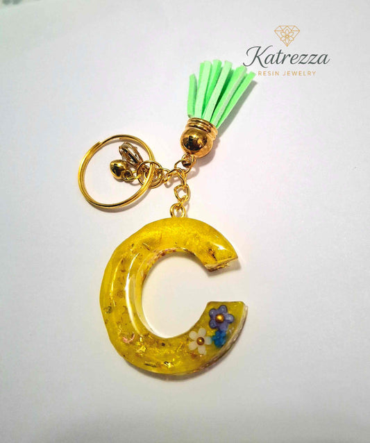 Yellow resin letter C keychain with gold flakes and tiny flower charms, attached to green tassel and gold keyring.