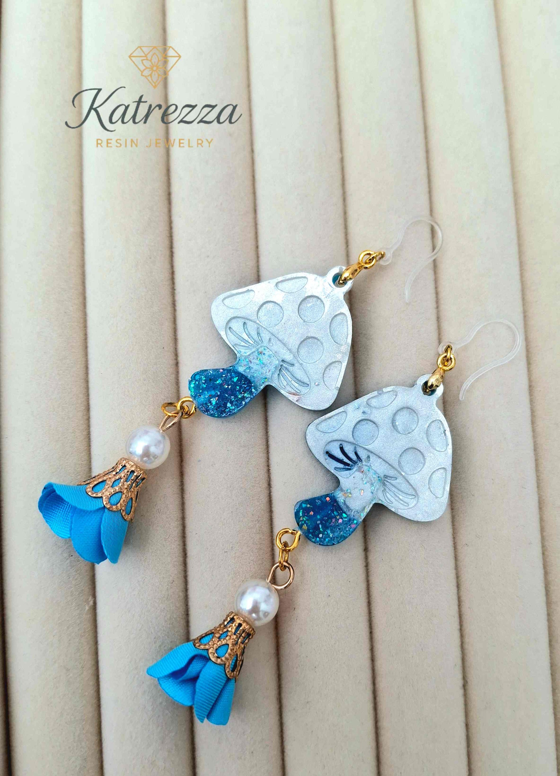 "Close-up of double-sided resin mushroom earrings showing glittery blue stems and textured white caps – Katrezza Jewelry"
