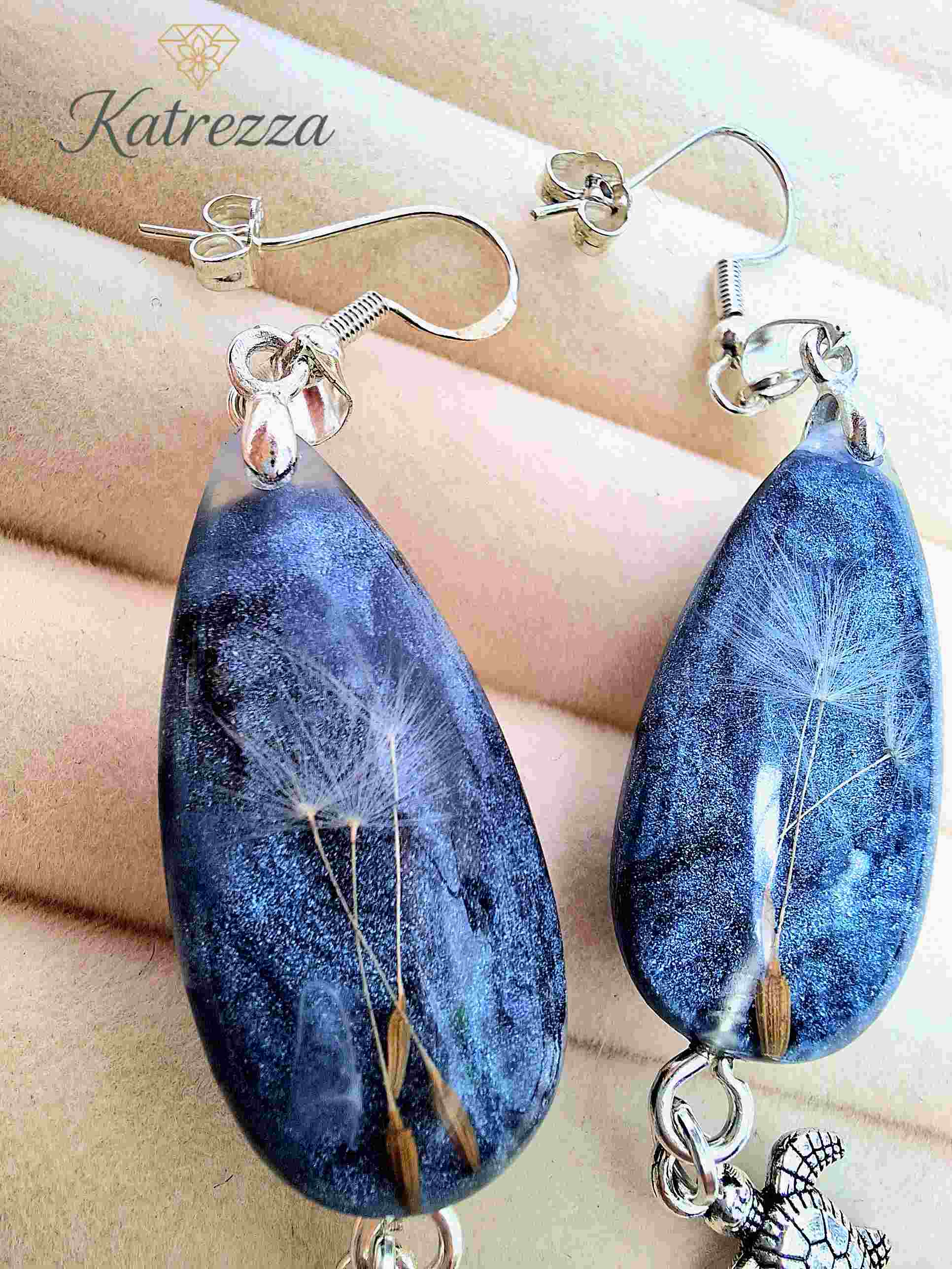 Close-up of handmade resin drop earrings with dandelion bouquet inside blue glitter resin