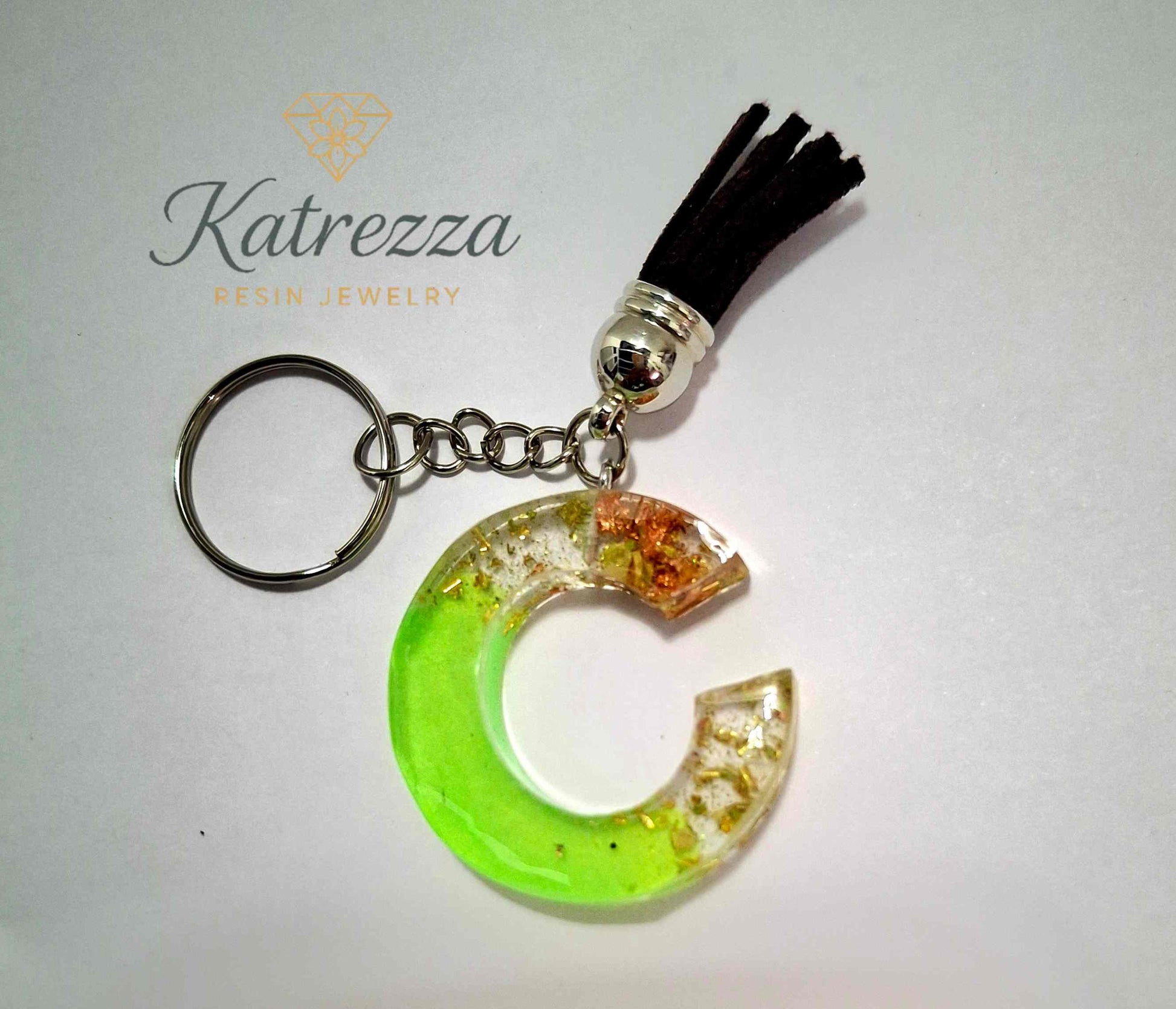 Green resin letter C keychain with black tassel and silver ring, decorated with gold and copper foil.
