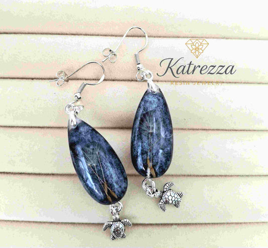 Close-up of handmade resin drop earrings with dandelion bouquet inside blue glitter resin.
