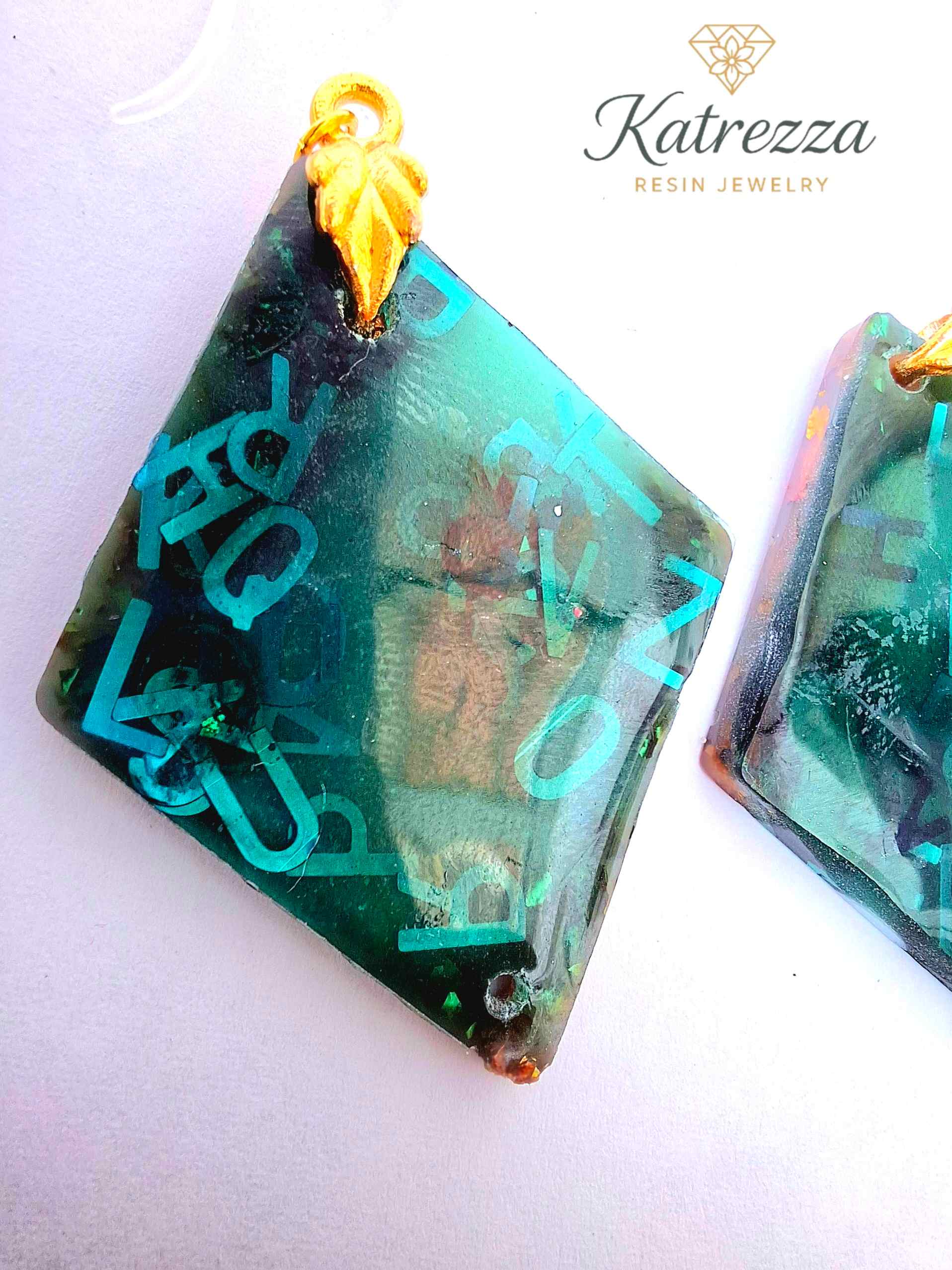 “Green resin earrings with shimmering blue letters and embedded details, geometric double-sided design.”